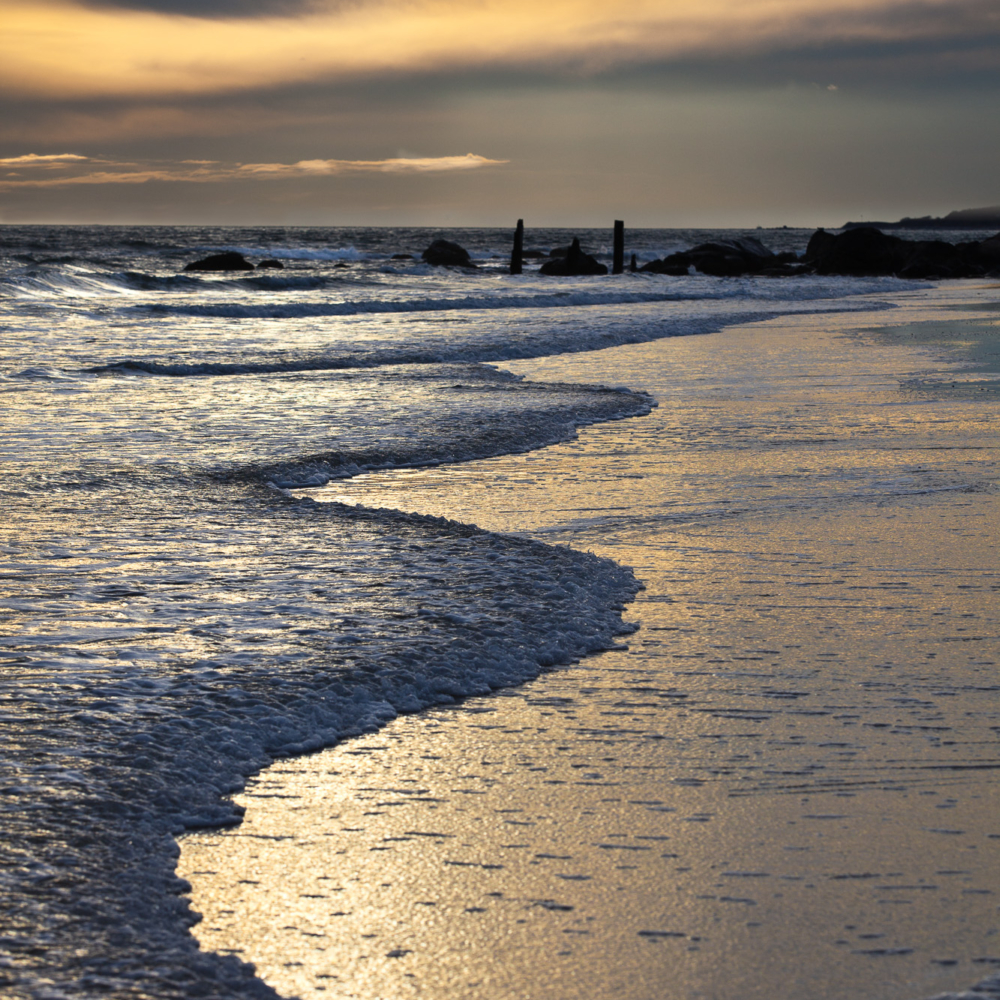 Waves lap shore with golden hue at sunset Napatree Point